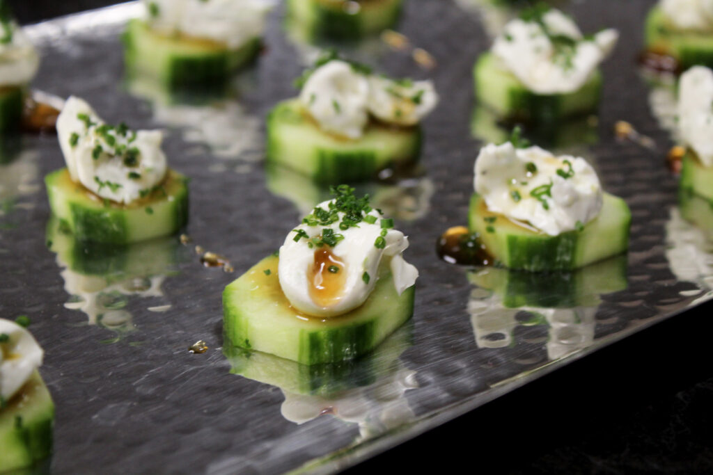 Platter of English cucumber slices topped with citrus whipped cheese and balsamic vinegar and chives